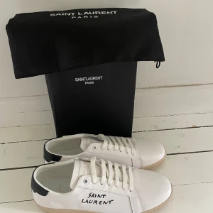 Saint Laurent vita  - Snygga vita sneakers från Saint Laurent med svart detalj på hälen och handskriven logga på sidan. Skorna är helt nya och om ni har några andra frågor så är de bara att höra av sig. Priset kan diskuteras vid snabb affär.
