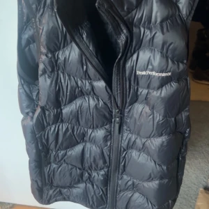  Peak Performance väst - Säljer en svart dunväst från Peak Performance. Västen har en dragkedja framtill och är perfekt för kyligare dagar. Den är stilren och funktionell med en quiltad design. Storlek 160 och endast använd ett fåtal gånger