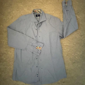 Blå skjorta från R2 Amsterdam - Tjo! Säljer en snygg skjorta från R2 Amsterdam. Den har snygga mönster vid krage och ärmar. Den har aldrig används av mig och om du har några frågor är det bara att ställa de!