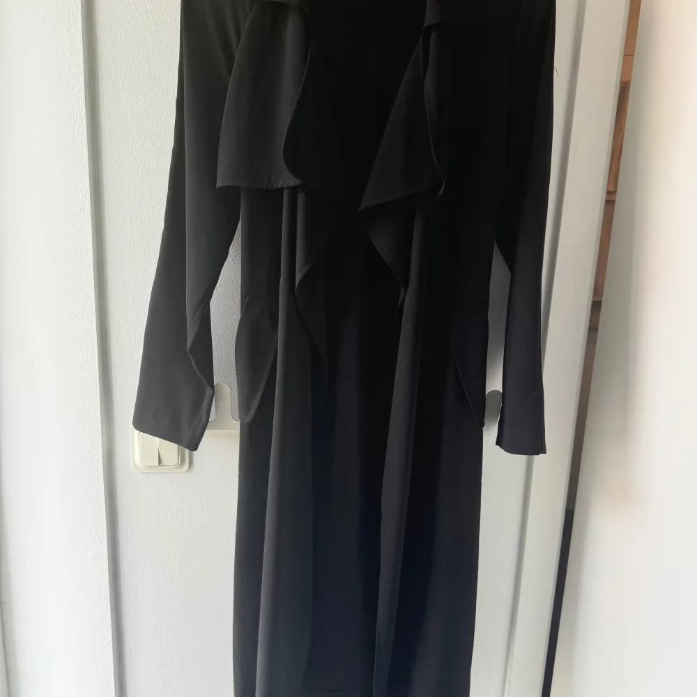 Säljer en elegant svart lång kappa från Bik Bok. Den har en stilren design med långa ärmar och ett snyggt fall. Perfekt för höst och vår, och kan enkelt stylas upp eller ner beroende på tillfälle. Kappan är inte fodrad utan den är i ett tunnare ”tyg material”. Takit.