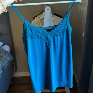 Blå linnetopp med spetsdetaljer - Snygg blå linnetopp spetsdetalj längs halsringningen. 