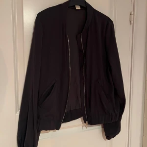 Mörkgrå bomberjacka från H&M - Mörkgrå bomberjacka från H&M med dragkedja framtill. Jackan har långa ärmar och två fickor. 