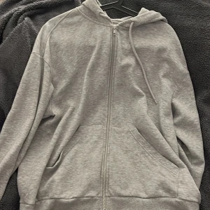 Grå hoodie från Monki - Säljer en stilren grå hoodie från Monki i storlek S. Den har dragkedja framtill och en bekväm huva med dragsko. Perfekt för en avslappnad look.