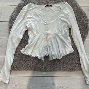 Vit långärmad topp från Gina tricot - Säljer en söt vit långärmad topp från Gina tricot Toppen har spetsdetaljer längs halsringningen och en liten rosett framtill. Skriv för fler bilder