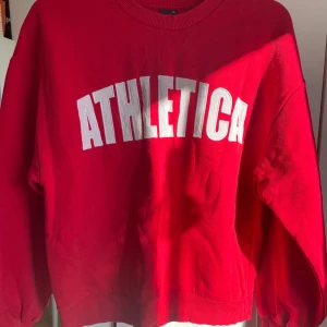 Röd sweatshirt från Gina Tricot! - Säljer en röd sweatshirt från Gina Tricot med texten 'ATHLETICA' i vitt på framsidan. Tröjan har en normal passform och ribbade muddar vid ärmslut och nederkant. Perfekt för en avslappnad stil. Jätte bekväm och fin💗
