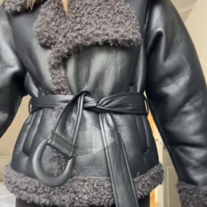 Svart skinnjacka med pälsdetaljer - Snygg svart skinnjacka med mjuka pälsdetaljer.  Jackan har ett bälte i midjan för en justerbar passform och långa ärmar. Liknar adoore jackan men är ifrån about you och märket ” Guido Maria Kretchemer” nypris 1699kr 