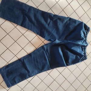 Blå jeansbyxor med snörning - Säljer ett par bekväma blå jeansbyxor med elastisk midja och snörning. Byxorna har en avslappnad passform och raka ben, perfekta för en casual look. De har praktiska fickor fram och är tillverkade i ett mjukt denimtyg.