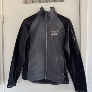 Grå och svart jacka från Westcoast - Säljer en stilren grå och svart jacka från Westcoast med broderad logga på bröstet. Jackan har dragkedja framtill och en praktisk ficka med dragkedja på ärmen. (Katt och kanin finns i hemmet)