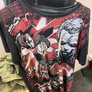 Svart och röd Superman t-shirt - Cool t-shirt med Superman-tryck i svart, rött och grått. Designen har en dramatisk serietidningsstil med text och en stor bild av Superman. Perfekt för fans av superhjältar!