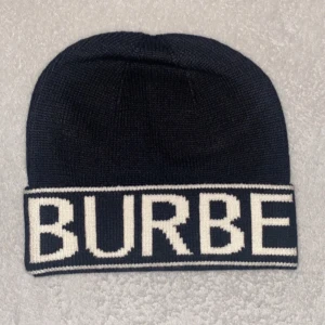 Svart stickad mössa från Burberry - Snygg svart stickad mössa från Burberry med vit textdetalj. Perfekt för att hålla värmen med stil under kyliga dagar.