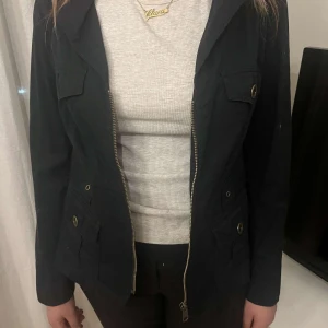 Svart jacka med dragkedja - Snygg svart jacka med dragkedja och knappar. Jackan har flera fickor och en klassisk krage.