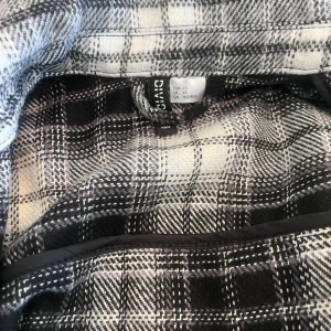 Svart och vit rutig overshirt från Divided - Säljer en stilren svart och vit rutig overshirt från Divided. Jackan har långa ärmar och knappar framtill. Perfekt för lager-på-lager under höst och vår. Två bröstfickor och sidfickor ger extra funktionalitet.