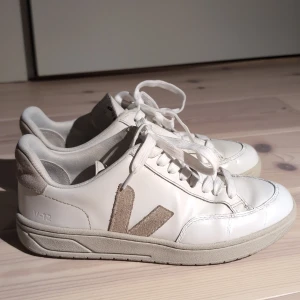 Vita sneakers från Veja - Säljer ett par stilrena vita sneakers från Veja med beiga detaljer i ett bra skick. Skorna är i storlek 38 men skulle även passa 39 då de är lite stora i storleken. Priset kan diskuteras! Nypris ca 2000