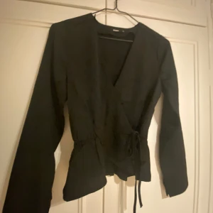 Svart långärmad blus från bikbok - En perfekt långärmad top för ett kalas eller när man ska klä sig fint. Silkesmaterial och volang. Har även en roset på sidan och den är V ringad