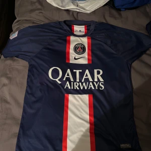  PSG fotbollströja - Hej Säljer denna blå PSG tröja med Mbappe på ryggen, tröjan är i storlek m vid frågor eller funderingar är det bara höra av sig!!