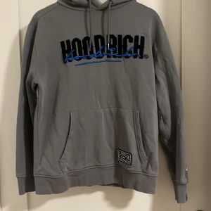 Grå hoodie från Hoodrich - Säljer en stilren grå hoodie från Hoodrich med svart och blå logga på bröstet. Tröjan har en praktisk magficka och justerbar huva med snören. Perfekt för en avslappnad streetwear-look. Den är storlek S men sitter som M. Köpt för 1100 och den är knappt använd. Pris kan diskuteras. 