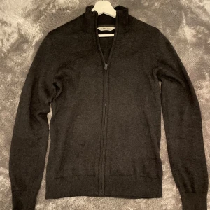 Svart kofta från 11 Project - Snygg svart kofta från 11 Project med dragkedja framtill. Perfekt för lager-på-lager och har en stilren design med ribbade muddar vid ärmslut och nederkant. Passar till många olika outfits. Den är i storlek S och 100% bomull.