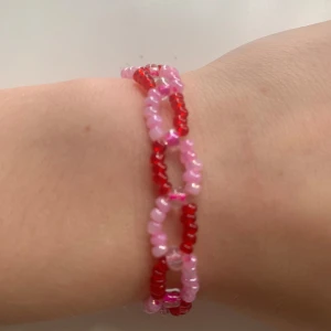 Rosa och rött armband - Charmigt armband med små pärlor i rosa och rött. Perfekt för att lägga till en färgglad touch till din outfit. Armbandet har ett enkelt och lekfullt mönster som passar bra till både vardag och speciella tillfällen. Kostar bara 15kr!