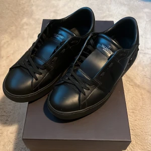 Svarta Valentino Garavani opens - Snygga svarta sneakers från Valentino Garavani med klassisk design och snörning. Skorna har en stilren look och är perfekta för en trendig stil. Levereras med extra skosnören och dustbags box ingår även. Skicket är 9/10, ända defekten är ett litet skav på högra skosulan.