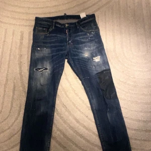 Blå jeans från Dsquared2 - Snygga blå jeans från Dsquared2 med slitna detaljer och en cool patch med '1975' på baksidan. De har en klassisk femficksdesign och en knappgylf. Perfekta för en avslappnad stil med en touch av edge.