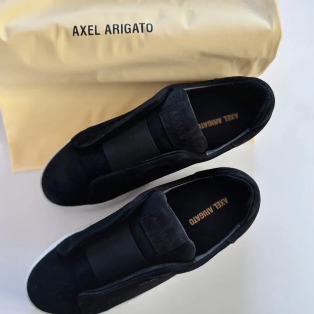 Snygga svarta sneakers från Axel Arigato med en stilren design. Skorna har en vit sula och är tillverkade i ett material som ger en lyxig känsla. Perfekta för en modern och trendig look.. Kengät.