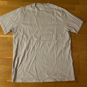 Ljuslila t-shirt från Woodbird - Säljer en stilren ljuslila t-shirt från Woodbird. Den har en diskret broderad logga på bröstet och är tillverkad i mjuk bomull. Perfekt för en avslappnad look. Passar både S, M och L då den är oversized