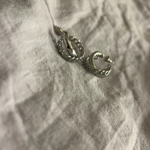 Silvriga örhängen med kedje design - Snygga silvriga örhängen med en unik kedje design. Perfekta för att ge en stilren touch till din outfit. De är små och lätta, vilket gör dem bekväma att bära hela dagen.