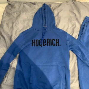 Blå Hoodrich hoodie och mjukisbyxor med snörning - Säljer ett set blå hoodie och mjukisbyxor från Hoodrich med snyggt tryck på benet. Byxorna har elastisk midja med snörning, ribbade muddar vid benslut och mjukt material som är skönt att ha på sig. Perfekt för chill eller streetwear-stil.