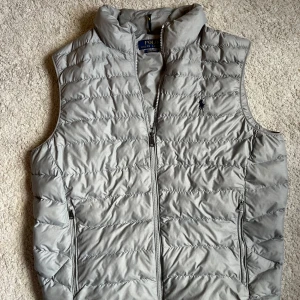 Grå dunväst från Polo Ralph Lauren - Snygg grå dunväst från Polo Ralph Lauren. Den är i nytt skick utan några deffekter! Storleken är M.