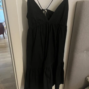 Svart kort klänning från Zara - Säljer en svart klänning från Zara i storlek M. Klänningen har tunna axelband som korsas i ryggen och en v-ringning fram med volang nedtill. Säljer då den inte kommer till användning💞