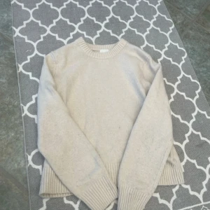 Cremevit stickad tröja från H&M - Mysig cremevit stickad tröja från H&M i storlek M. Tröjan har rund hals, långa ärmar och breda ribbade muddar. Enkel och clean design som är lätt att matcha med jeans eller kjol. Perfekt för kyliga dagar.