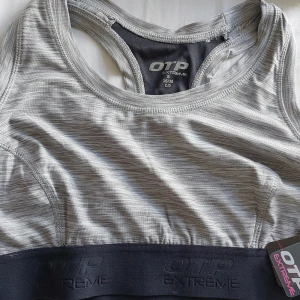 Sport BH small, C/D-kupa - Supersnygg grå BH-topp från OTP Extreme med mörkare grått band under bysten och diskret mönstrad yta. Toppen har brottarrygg och är perfekt för träning. Materialet är mjukt och stretchigt polyester som andas. Snygg logga framtill och på bandet.