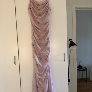 Lång blommig meshklänning från SHEIN - Säljer en superfin långklänning från SHEIN i storlek S. Klänningen är ljusrosa med blommigt mönster och har snygga draperingar längs hela längden. Materialet är mesh som ger en cool och luftig känsla. Perfekt för dig som gillar romantisk och trendig stil. Aldrig använd
