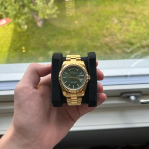 Seiko mod Day-Date klocka - Helt ny! Snygg Seiko Oyster Perpetual Day-Date med grön urtavla och guldigt armband i metall. Klockan har dag- och datumvisning, räfflad bezel och transparent baksida som visar urverket. Diameter 39mm. Lågt problemet pris då det finns ett märke som syns under starkt ljus! Frågor? Skicka dm!
