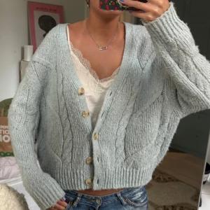 Ljusblå stickad kofta med knappar - Supermysig ljusblå stickad kofta med grova flätstickade detaljer och stora träknappar framtill. Koftan har en loose passform, v-ringning och långa ärmar. Perfekt att slänga över en topp för en chill och snygg look.