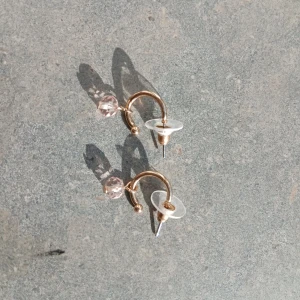 Guldiga örhängen med rosa pärla - Snygga små örhängen i guldfärgad metall med en rund, ljusrosa pärla som hänger i botten. Designen är enkel men ändå unik med en öppen cirkelform och transparent bakstycke. Perfekta för att ge din look lite extra glans.