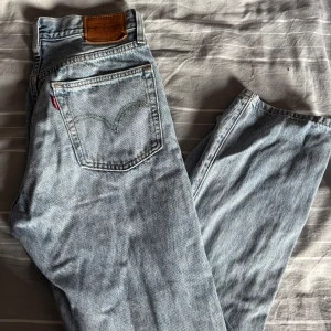 Levi's 501 ljusblå jeans - Ljusblå Levi's 501 jeans med klassisk femficksdesign och knappgylf. Jeansen har raka ben och medel hög midja, tillverkade i slitstarkt bomullsdenim. Snygga kontrastsömmar och den ikoniska läderpatchen baktill. Perfekta för en chill och tidlös look. Använda fåtal gånger. 