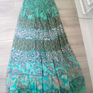 Turkos långklänning med mönster - Säljer en bohemisk långklänning i turkos med färgstarka mönster och paisley-detaljer. Perfekt för dig som gillar färg och unika printer. Den är köpt i Barcelona och har använts två gånger så den är i väldigt bra skick! Eftersom den är i så bra skick och för att jag köpte den för 1000 kr så kommer jag sälja den för 700-800 kronor men priset kan diskuteras. Det finns ingen speciell storlek men skulle säga att den passar alla som har storlek S och över och till och med kanske storlek Xs. 