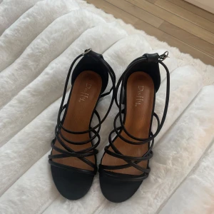 Snygga svarta klackskor!🖤 - Snygga svarta sandaler från Duffy med chunky klack och flera tunna remmar som korsar över foten. Skorna har öppen tå och spänne vid ankeln. Perfekt för dig som gillar stilrena och trendiga skor med lite höjd. Materialet är syntet och sulan är platt framtill.💕😝