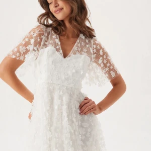 Vit blommig kortklänning med spets Student klänning - Superfin vit kortklänning med v-ringning och transparenta spetsärmar. Klänningen har 3D-blommor över hela tyget och ett flowigt fall. Perfekt till student eller sommarens alla tillfällen. Söt och romantisk vibe med blommigt mönster och spetsdetaljer. Nypris 999kr, använd en gång!!