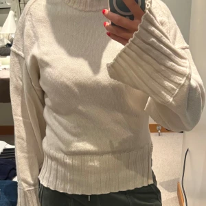 Beige stickad tröja med ribbade detaljer från Arket - Säljer en beige stickad tröja med breda ribbade muddar vid ärmslut och nederkant. Tröjan har rund hals och långärmade ärmar med lite loose passform. Perfekt för dig som gillar enkel och clean stil med snygga detaljer.