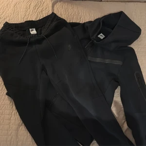 Nike tech  - Svarta mjukisbyxor från Nike med slim passform och snygg snörning i midjan. Byxorna har diskret Nike-logga på benet och är gjorda i mjukt och bekvämt material, perfekta för chill eller träning. Tidlös design med ribbade muddar vid benslut.