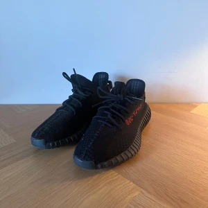 Adidas Yeezy Boost 350 V2 Black Red - Säljer ett par Adidas Yeezy Boost 350 V2 i svart med röd SPLY-350 text på sidan. Skorna är i storleken 44. Skorna har en stickad ovandel, snörning och en grym boost-sula för maxad komfort. Perfekt för dig som gillar streetwear och vill ha något som sticker ut.