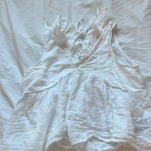 Vit blus med volang från Gina Tricot - Supersöt vit blus från Gina Tricot i luftig bomull. Blusen har volangdetaljer vid axlarna och v-ringad hals med knyt framtill. Den är ärmlös och har en flowy, lätt rynkad nederdel som ger en chill och romantisk vibe. Perfekt för varma dagar och sommarhäng. Har inte Använt den nån gång den e ny för att glömde testa den när jag köpte den och den var för liten för mig hoppas att den kommer till användning av någon annan 🥰
