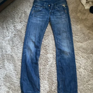Replay blå jeans straight fit - Klassiska Replay jeans i blå tvätt med raka ben och fem fickor. Snyggt slitna detaljer och ikonisk Replay-lapp bak i midjan. Jeansen har normal passform och är tillverkade i robust bomullsdenim. Perfekta för dig som gillar tidlös streetstil.
