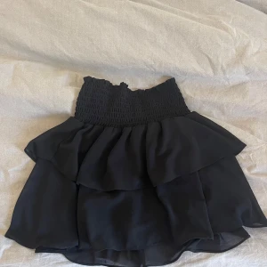 Svart volangkjol från Chelsea XXS - Supersöt svart kortkjol från Chelsea i storlek XXS. Kjolen har en smockad midja och dubbla volanger.