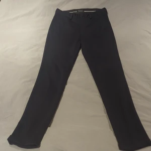 Marinblå kostymbyxor Selected Homme XS - Snygga svarta kostymbyxor från Selected Homme i storlek XS. Byxorna har en slim och skinny passform med klassisk midja och bälteshällor. Perfekta för en clean och stilren look, tillverkade i ett mjukt material som känns bekvämt hela dagen.