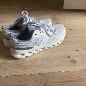 On clouds skor - Säljer ett par fräscha On Cloudtec sneakers i vitt och grått med cool, chunky sula och snygga detaljer. Skorna har meshpaneler för bra ventilation och snörning framtill. Perfekt för dig som gillar sportig stil och vill ha bekväma skor med unik design.