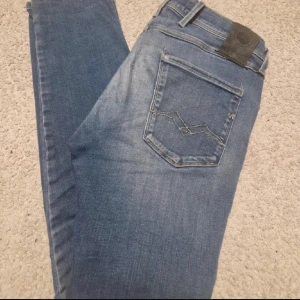 Replay blå jeans herr 29/30 - Säljer ett par snygga blå jeans från Replay i klassisk tvätt. Modellen har fem fickor, diskreta slitningar och raka ben. Jeansen är tillverkade i bomull och har Replay-logga på bakfickan. Perfekta för dig som gillar en tidlös look.