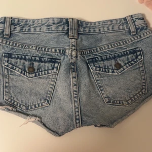 Lågmidjade Pull & bear shorts med fickor på bakfickan - Lågmidjade korta blåa shorts med slitningar från pull & bear. Storlek 40 och passar folk med storlek M.